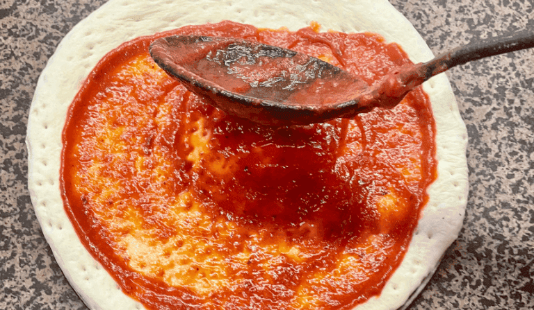 Étape de préparation d'une pizza avec étalage de la sauce tomate maison sur la pâte à l'aide d'une louche