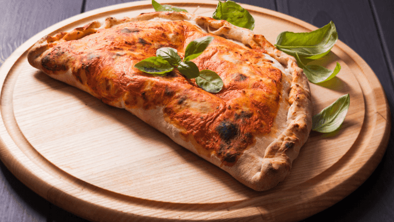 Calzone cuite au four sur planche en bois, dorée et décorée de basilic frais