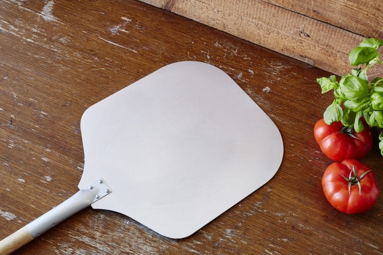 pelle a pizza poser sur un plan de travail a coté de tomate et basilic