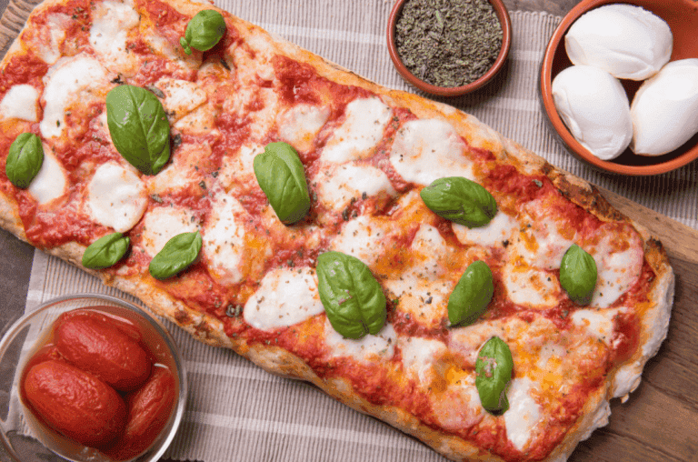 pizza cuite soupoudrer d'origan poser sur une planche avec plusieurs ingrédient autour mozza, tomate et origan.