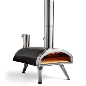 Four à pizza Ooni Fyra allumé avec flamme visible, design compact et moderne en acier inoxydable, vue de trois quarts.