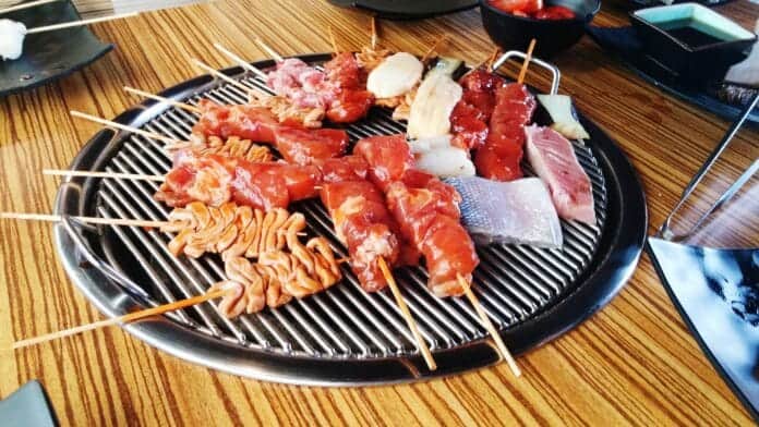 Sélection de brochettes de viande et de fruits de mer crus placés sur un grill circulaire dans un restaurant de barbecue coréen.
