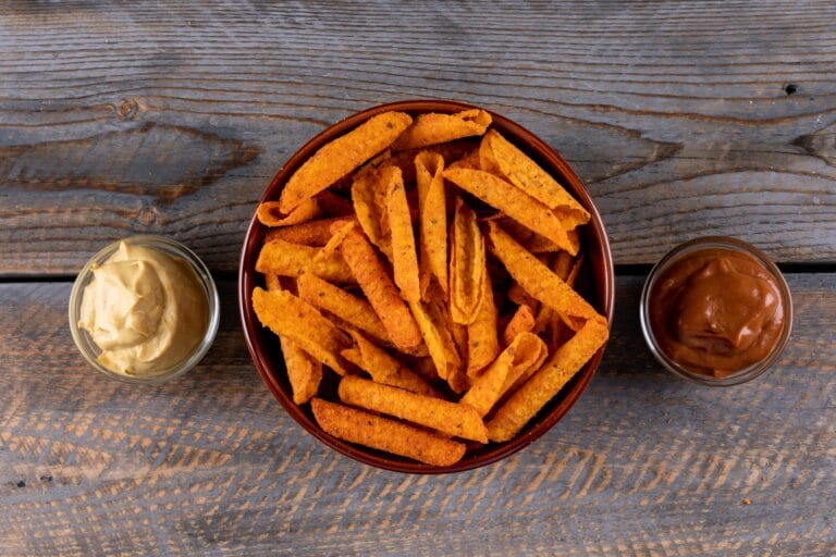 Vue du dessus d’un bol de frites de patate douce dorées cuites au Air Fryer, accompagnées de sauces maison sur table en bois rustique.