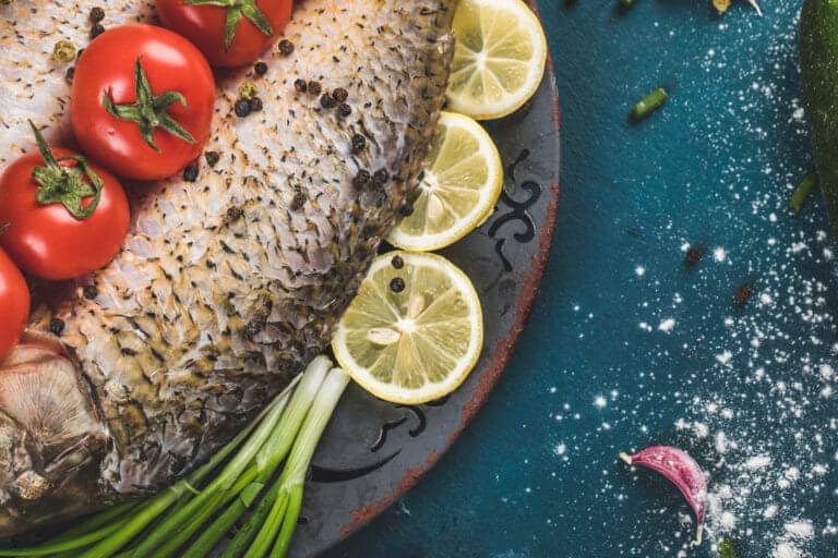 Poisson entier prêt à cuisiner avec rondelles de citron, tomates et herbes fraîches pour une recette black bass.