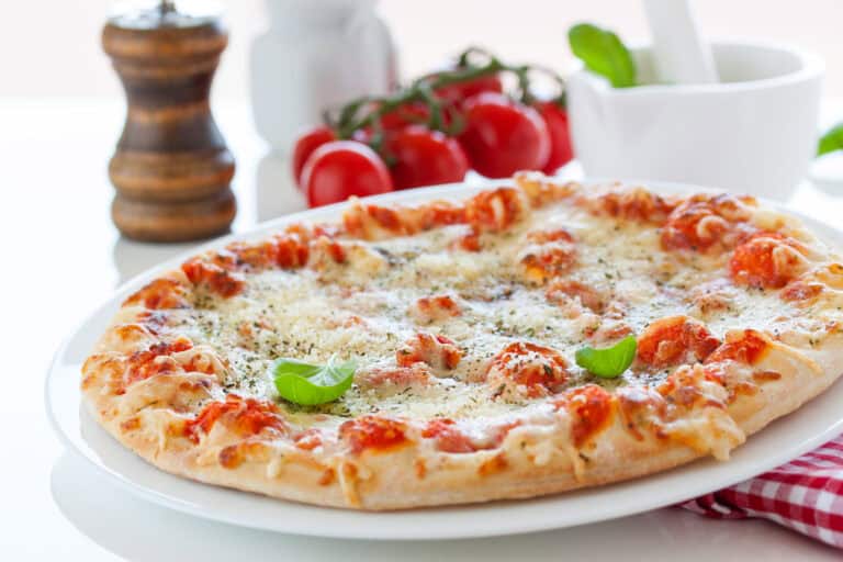 Pizza Margherita légère garnie de mozzarella fondue, tomates fraîches et basilic sur assiette blanche