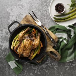 Faisan rôti en cocotte fonte avec asperges et carottes, peau dorée et chair fondante