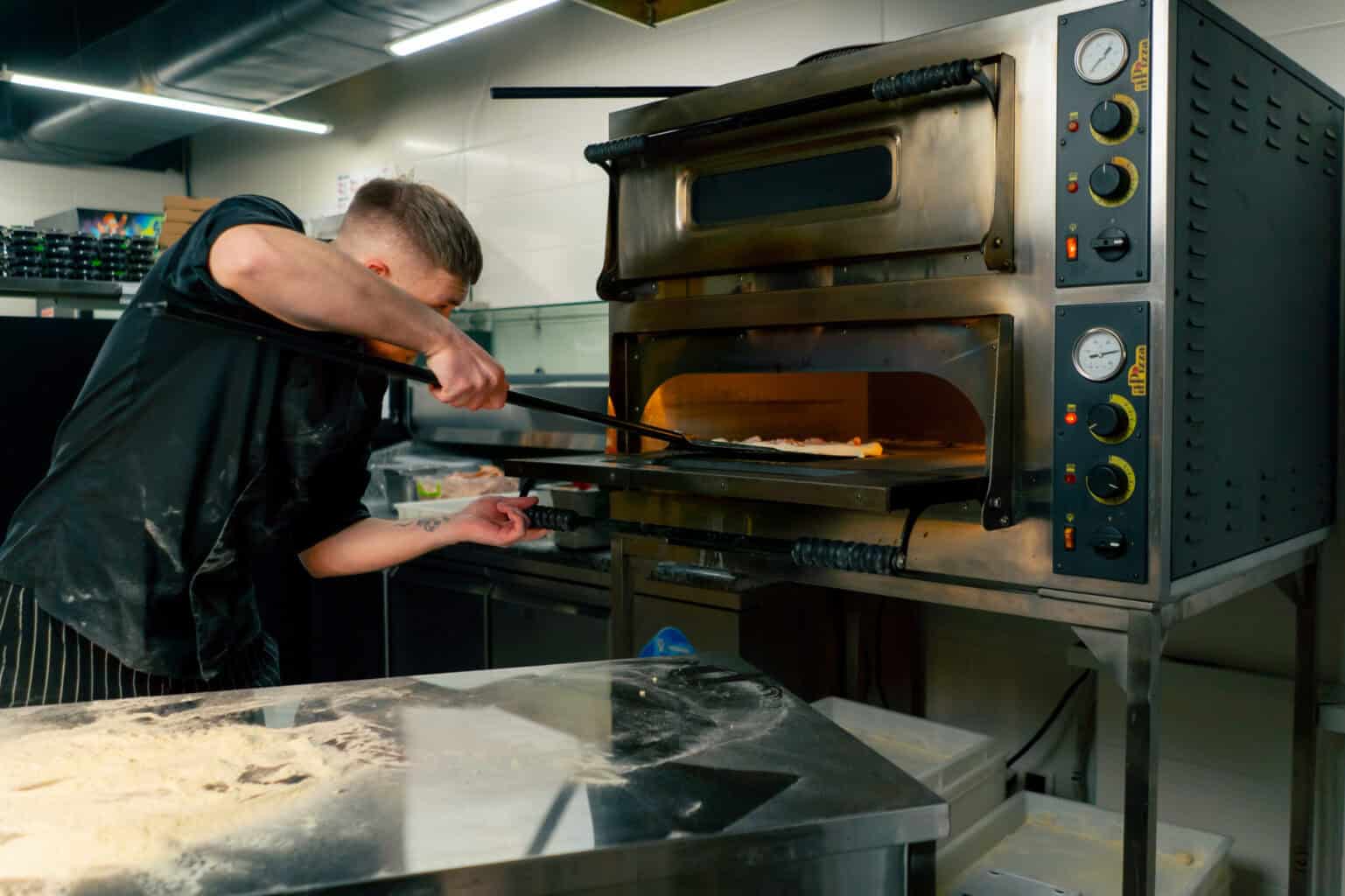 Chef manipulant une pelle pour cuire une pizza dans un four professionnel en acier de type four à pizza pro.