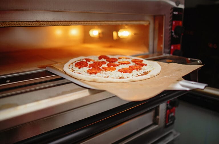 Pizza pepperoni placée sur une pelle prête à enfourner dans un four pizza électrique professionnel chauffé.