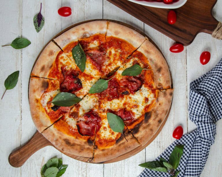 Pizza napolitaine cuite au four, tranchée sur planche en bois, garnie de sauce tomate, mozzarella fondue, basilic frais et charcuterie, avec tomates cerises autour