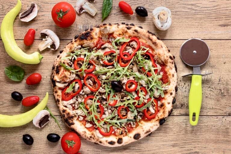 Pizza végétarienne avec poivrons rouges, roquette, champignons et olives sur fond en bois