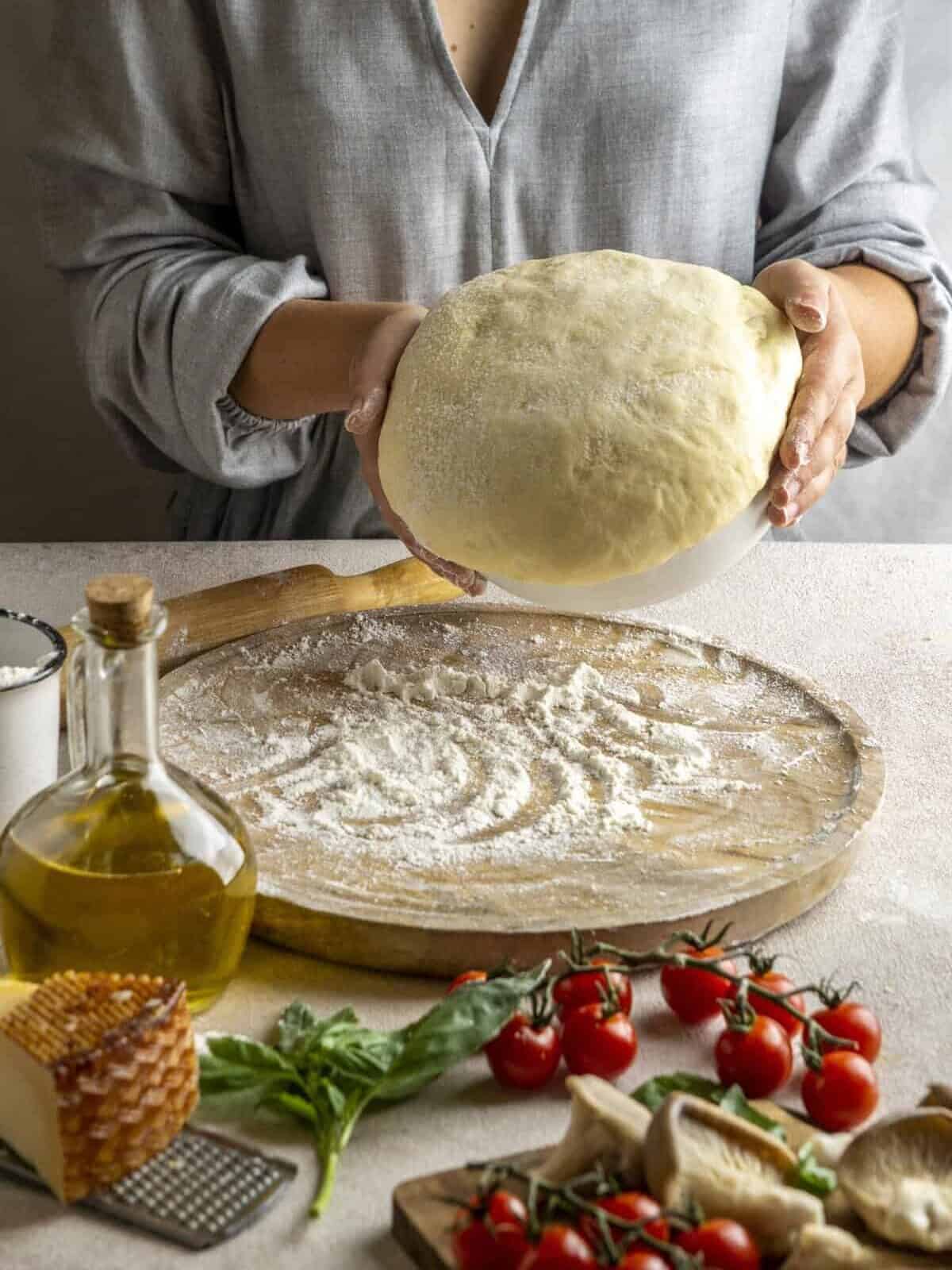boule de pâte pizza Thermomix posée sur un plan fariné avec sauce tomate, tomates fraîches et huile d’olive