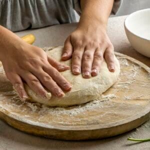 personne tenant une pâte pizza Thermomix bien levée au-dessus d’un plan fariné avec huile d’olive et tomates cerises