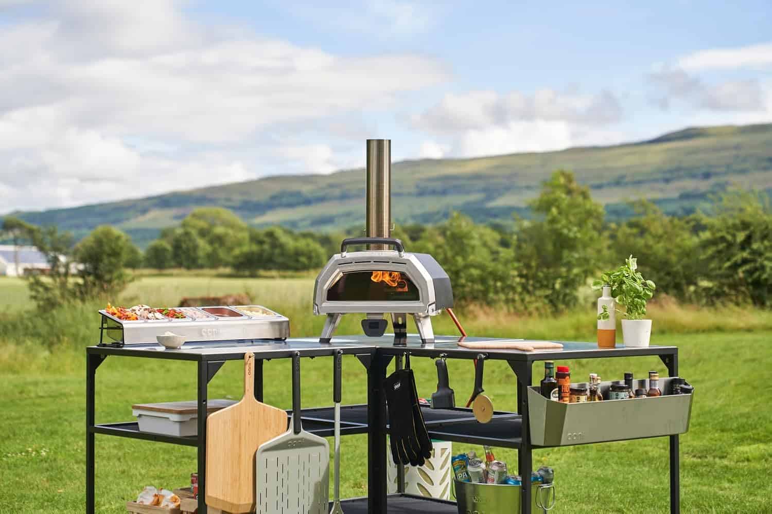 Ooni Karu 16 installé sur une table extérieure avec accessoires et ingrédients pour préparer des pizzas