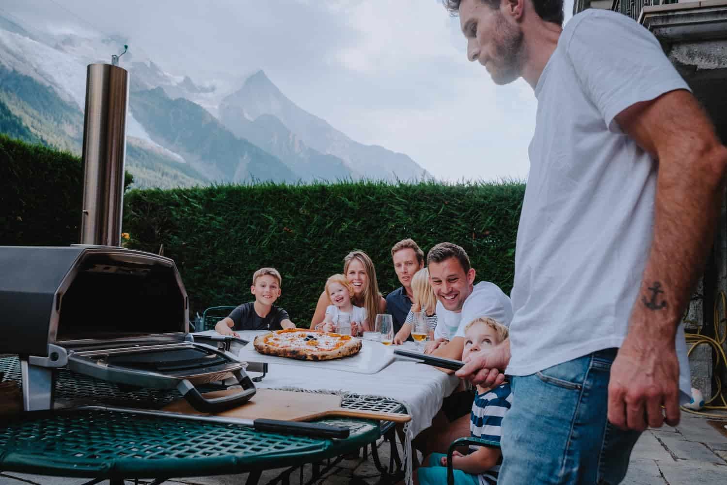 Utilisation du Ooni Karu 16 en terrasse avec une pizza sur pelle et des personnes autour d’une table