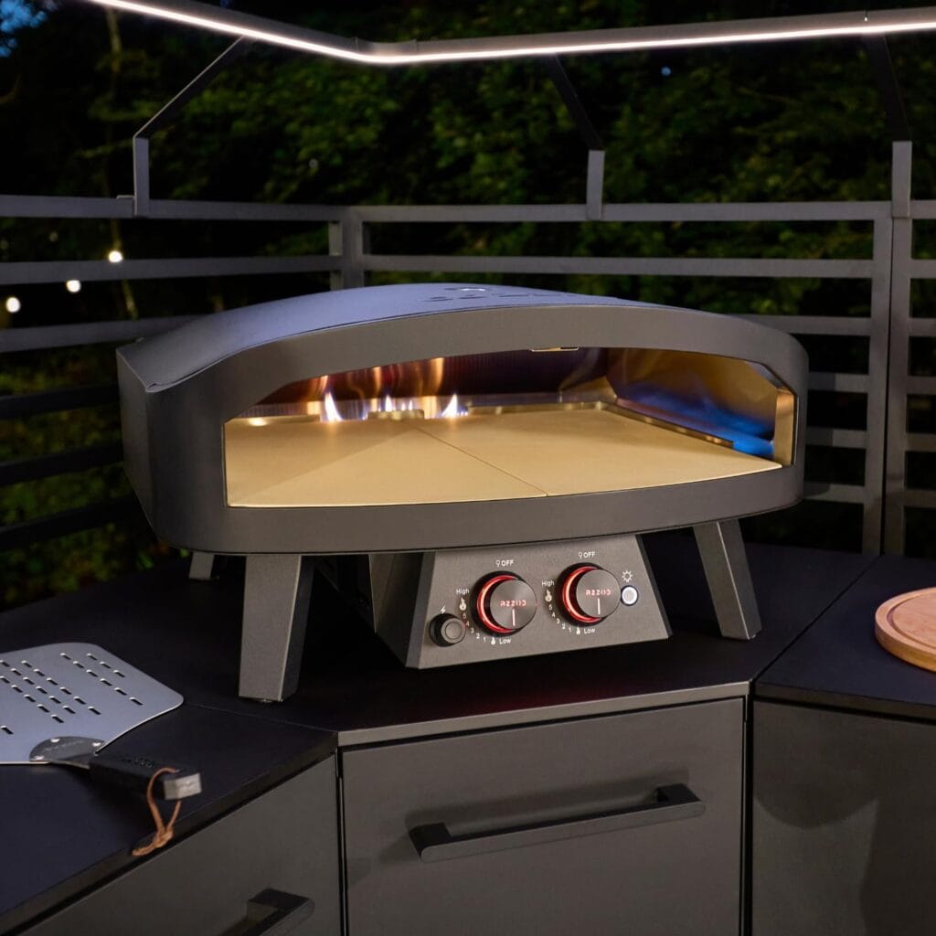 Four pizza Cozze 24" Black Edition : l'excellence du gaz sur une cuisine extérieure avec flammes visibles et commandes de température.